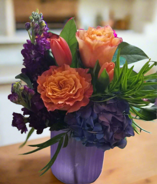 Colorful bouquet of flowers in a purple vase on a kitchen counter.